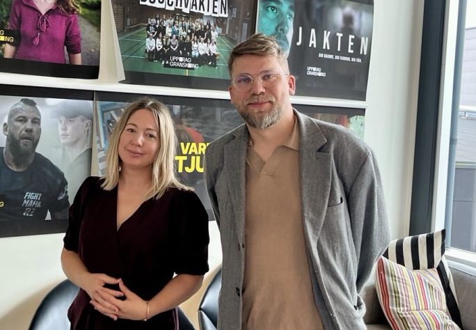 Jennifer tillsammans med ordförande för CUJ på ett kontor i SVTs lokaler, med affisher i bakgrunden med Uppdrag gransknings avslöjanden